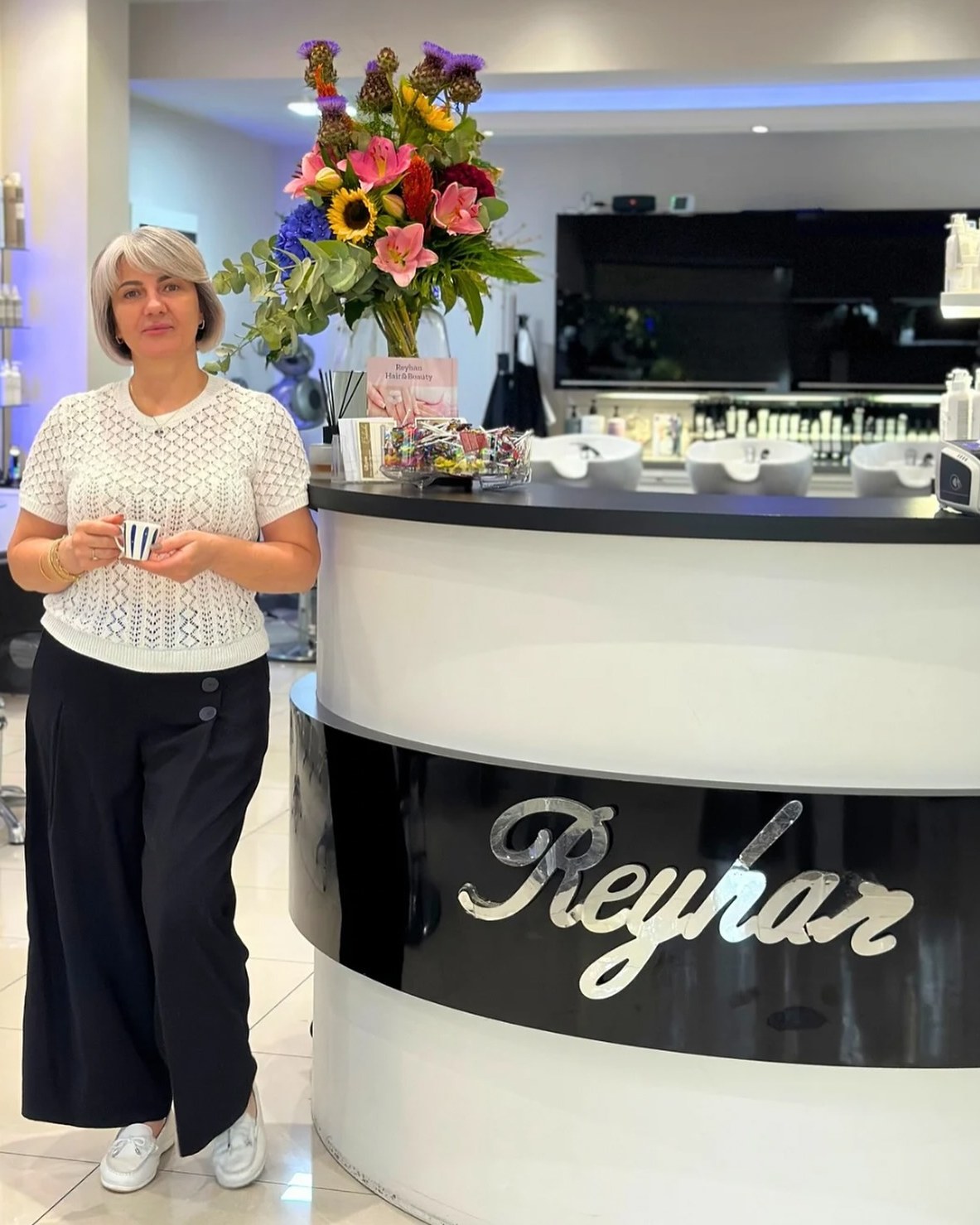 Reyhan bij de balie van haar salon, met een grote bos bloemen